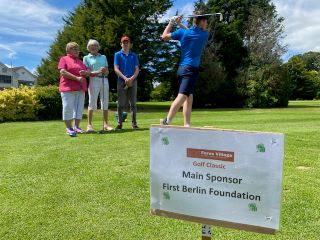 Golfers in the background watching a fellow golfer in full swing.  Picture in the foreground showing round sponsor 