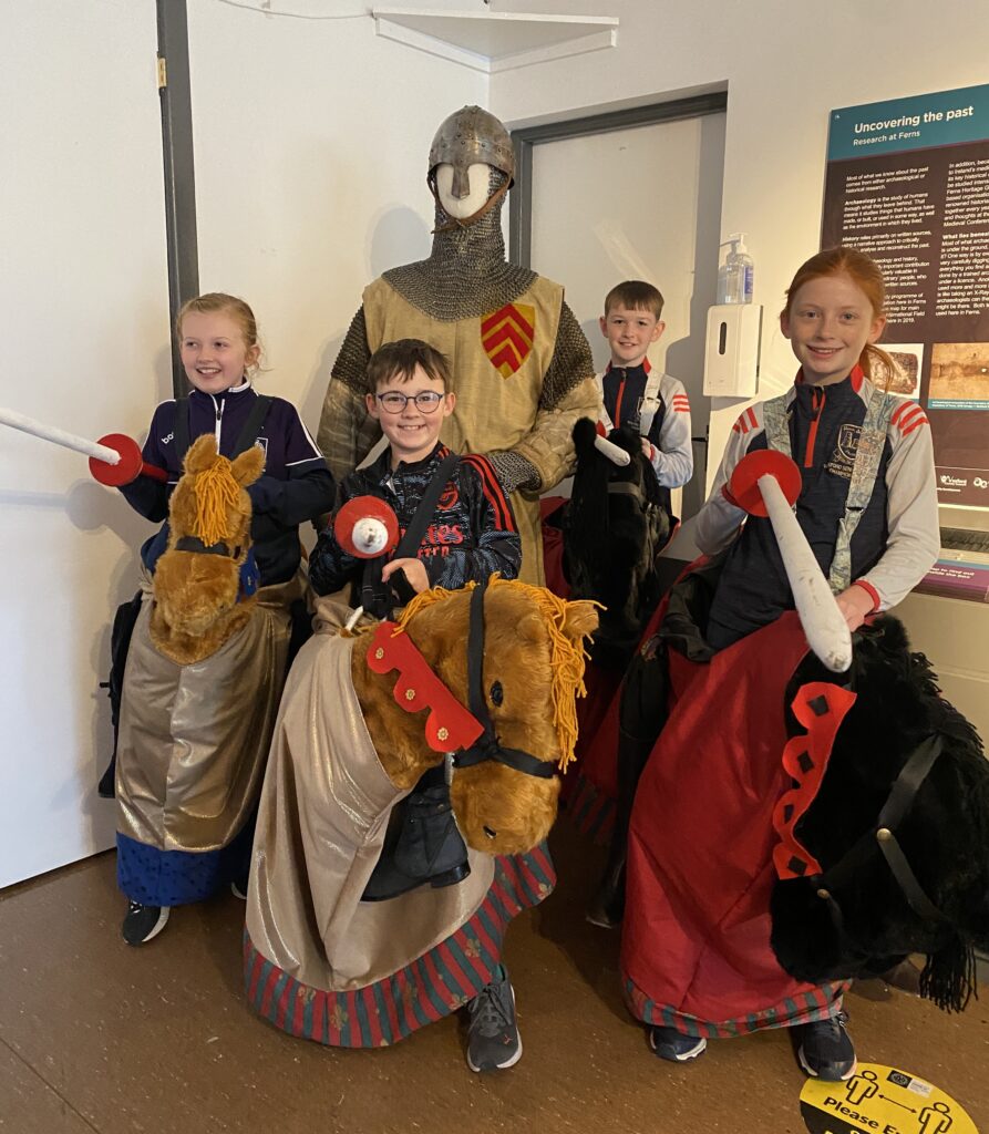 4 children in pantomime horses with jousting lances, standing in front of a mannequin in medieval knights costume  at the Medieval Ferns Experience 